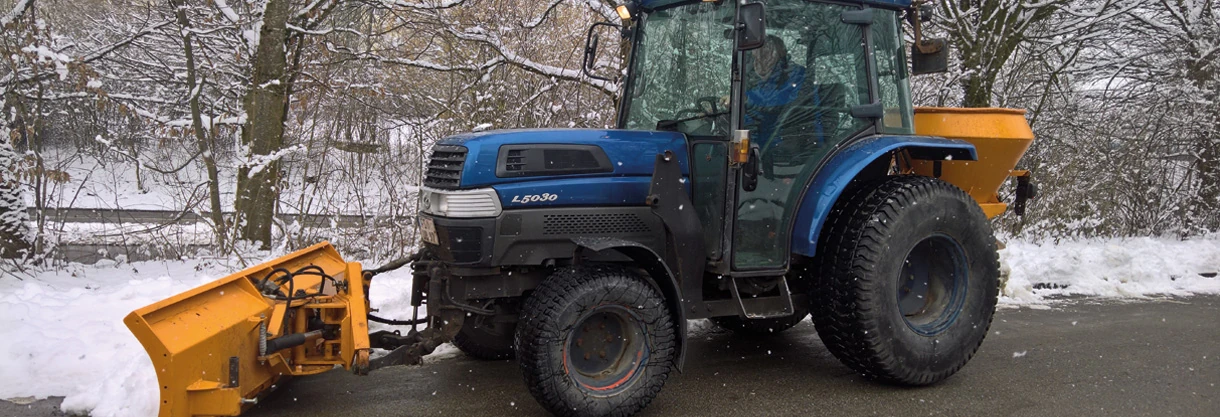 Traktor mit Räumschild und Streuer im Winterdienst